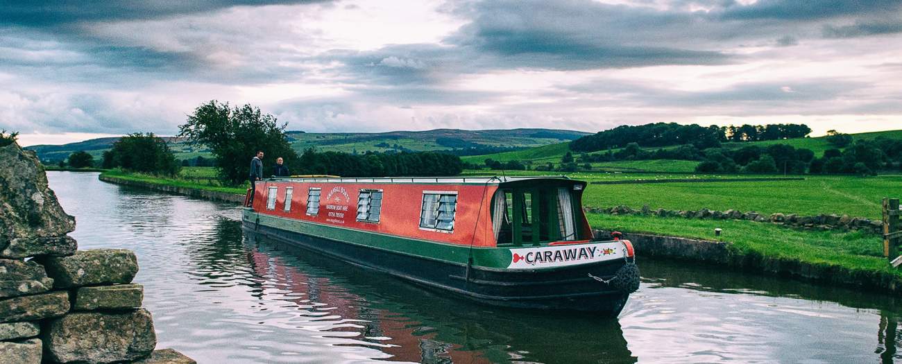The Snaygill narrowboat Caraway cruising the Leeds & Liverpool Canal between green Dales fields