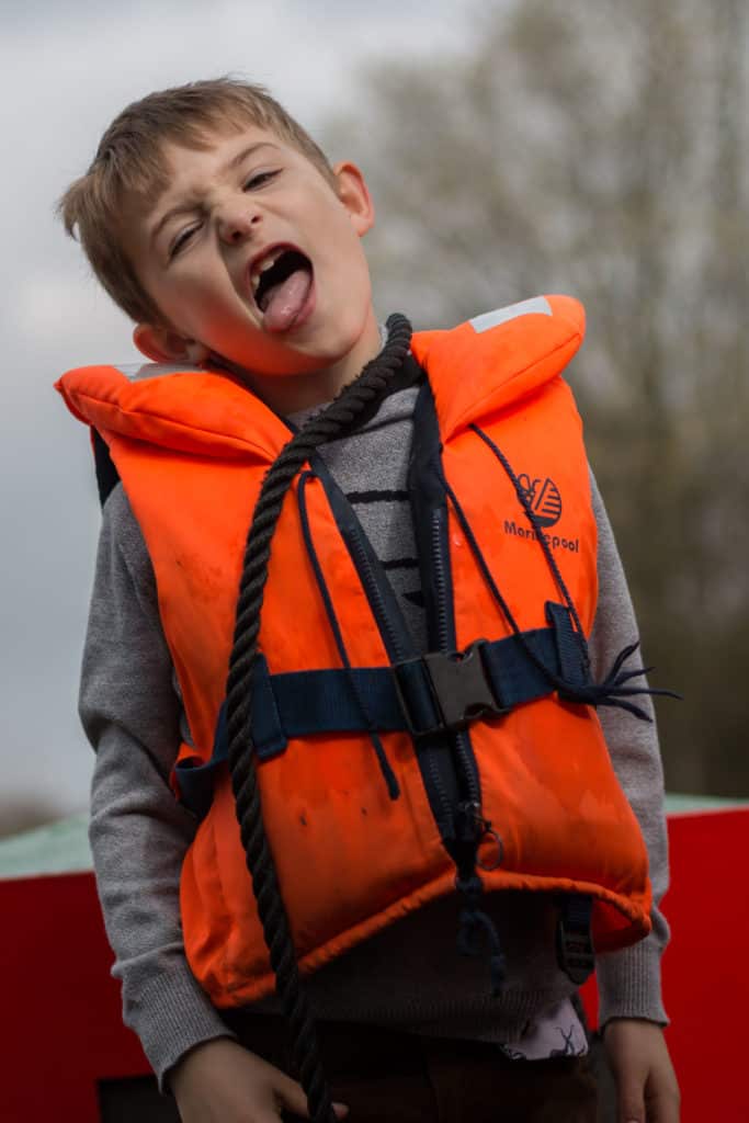 A young boy in an orange buoyancy aid larking about on deck
